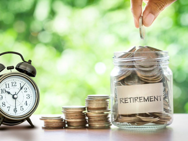 Hand putting Coins in glass jar with retro alarm clock , retirement