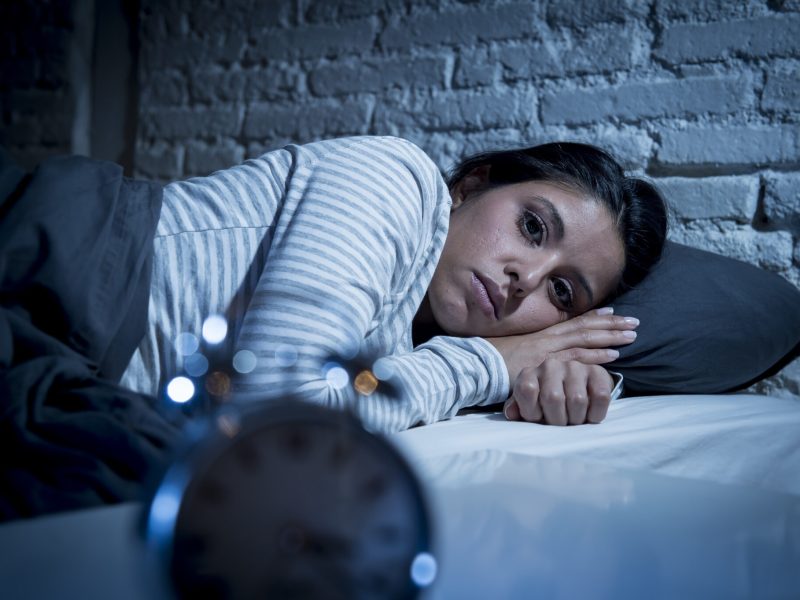 hispanic woman at home bedroom lying in bed late at night trying to sleep suffering insomnia