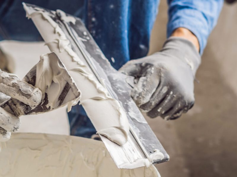 master is applying white putty on a wall and smearing by putty knife in a room of renovating house in daytime BANNER, long format