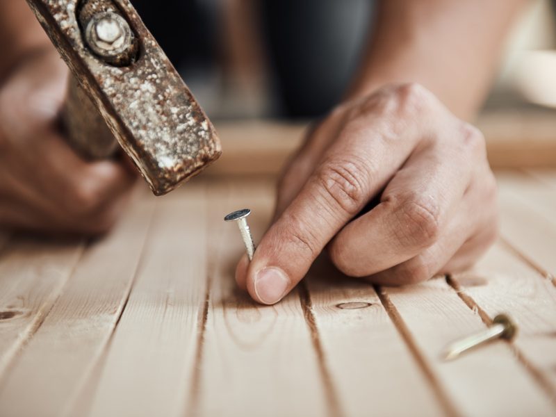 Close-up of handyman hammering a nail in wooden board. Concept of repair and renovation.