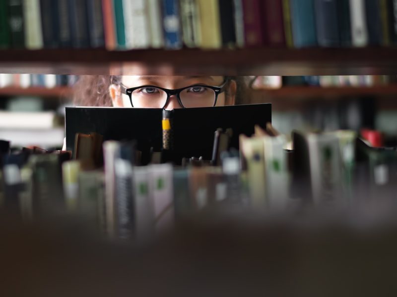 Portrait of clever student with open book reading it in college library