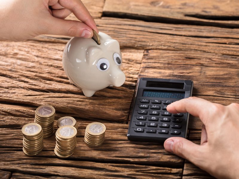 Person Calculating On Calculator With Coins And Piggy Bank