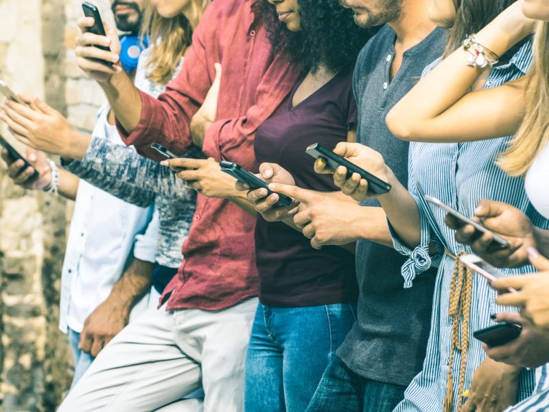 Group of multicultural friends using smartphone outdoors - People hands addicted by mobile smart phone - Technology concept with connected men and women - Shallow depth of field on vintage filter tone