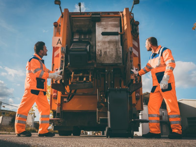 Two refuse collection workers loading garbage into waste truck e