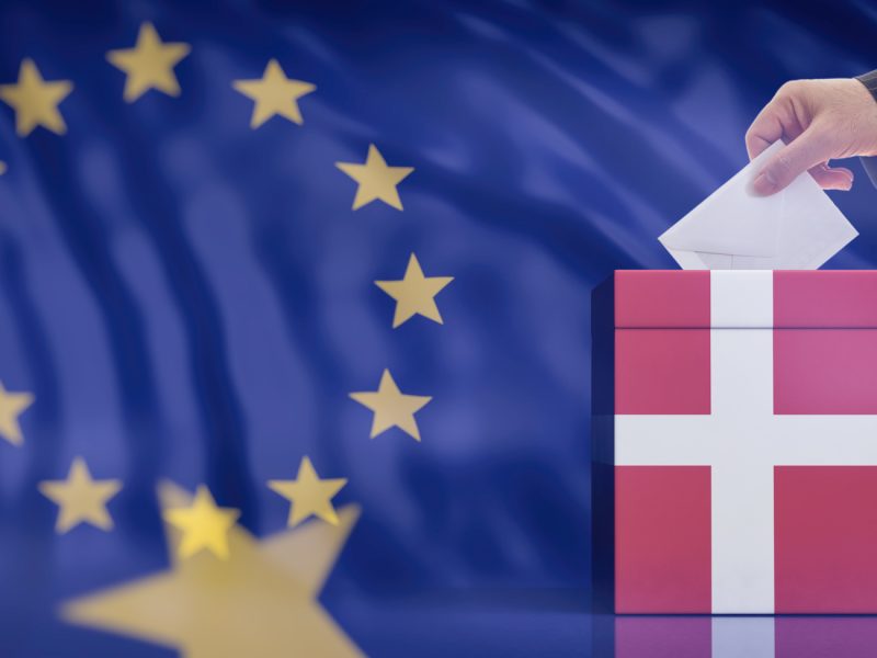 Hand inserting an envelope in a Denmark flag ballot box on European Union flag background. 3d illustration