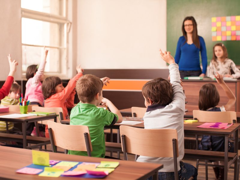 Children in elementary school are raised hand in clasroom