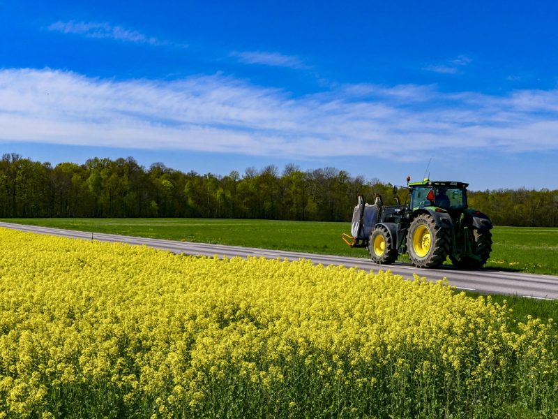 Farjestaden, Oland, Sweden May 10, 2020 An agricultural tractor driving on a back road next to a field of rapeseed.