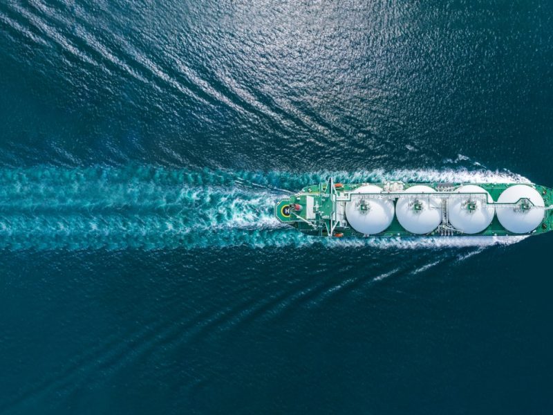 Aerial top view LNG Tanker ship (Liquified Natural Gas) with contrail in the ocean sea ship carrying container and running for export from container international port to custom ocean concept freight shipping by ship service