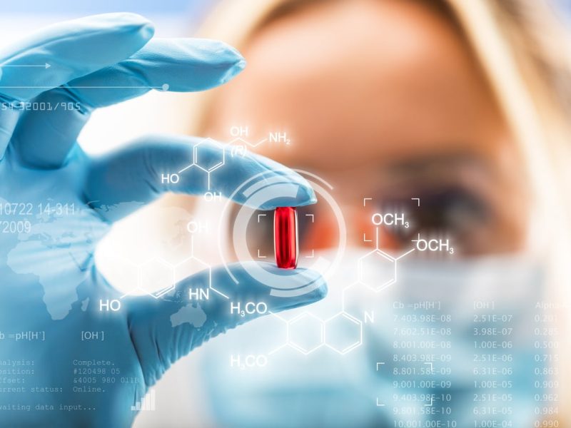 Young attractive female scientist holding a red transparent pill with futuristic scientific air interface with chemical formulas and research data in the foreground