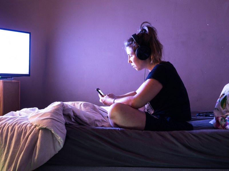 Young woman watching movie on television in bed at night. Teenage girl at home in her modern bedroom with headphones and digital tablet.