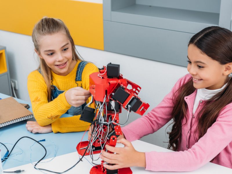 smiling schoolgirls touching red handmade robot in stem class