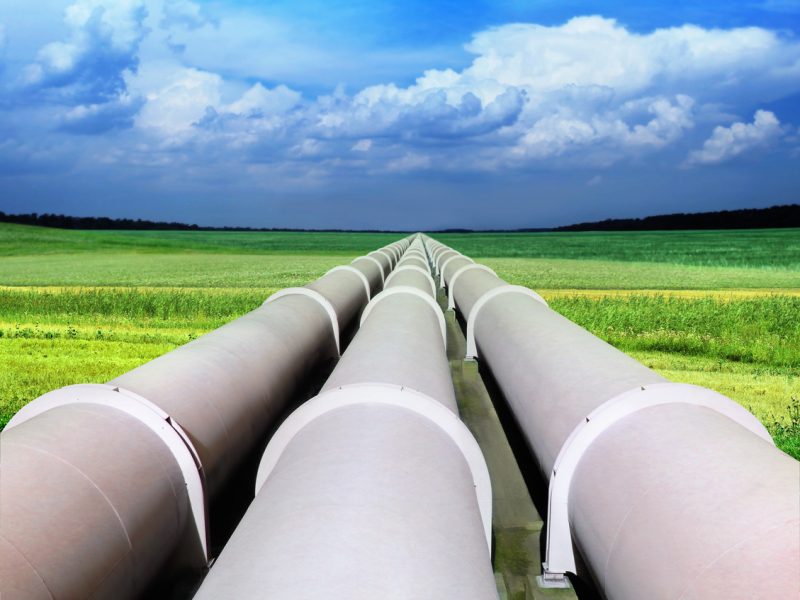 Three gas pipelines in a green field with blue sky