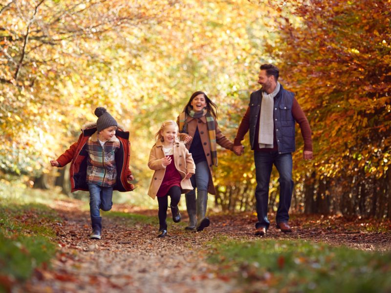 Family Walking Along Track In Autumn Countryside With Children Running Ahead