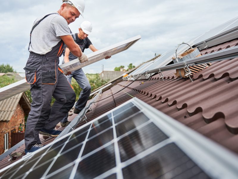 Man worker mounting solar panels on roof of house.