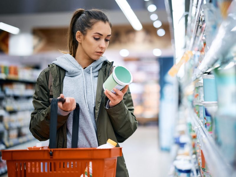 Young woman reading nutrition label while buying diary product in supermarket.