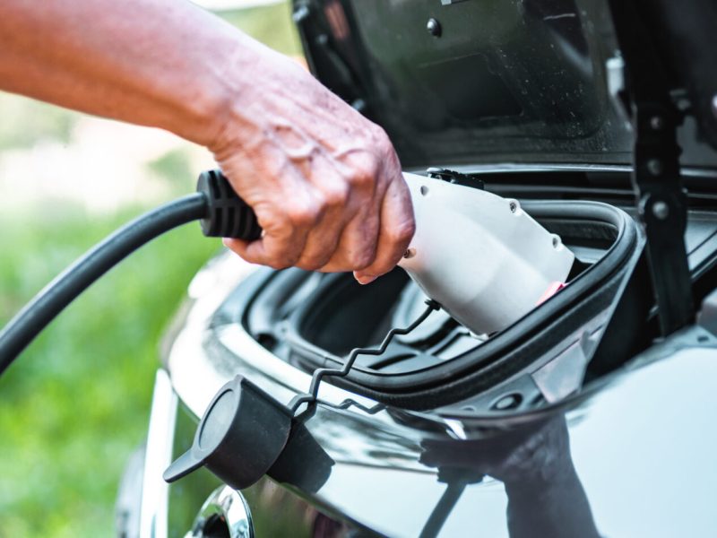 Human hand is holding electric car charging connect to electric car