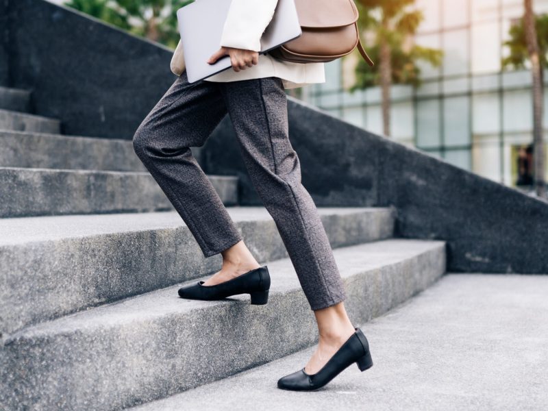 Close up legs of businesswoman hurry up walking she is late time Female business people holding laptop go to office in the modern city foot step on staircase