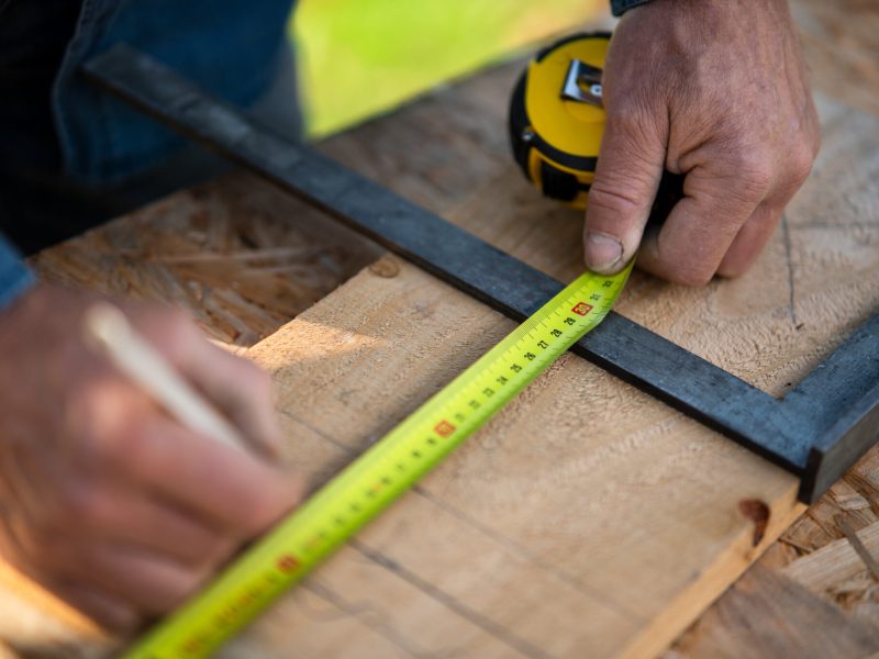 Close-up of handyman measuring a board, outside in garden.