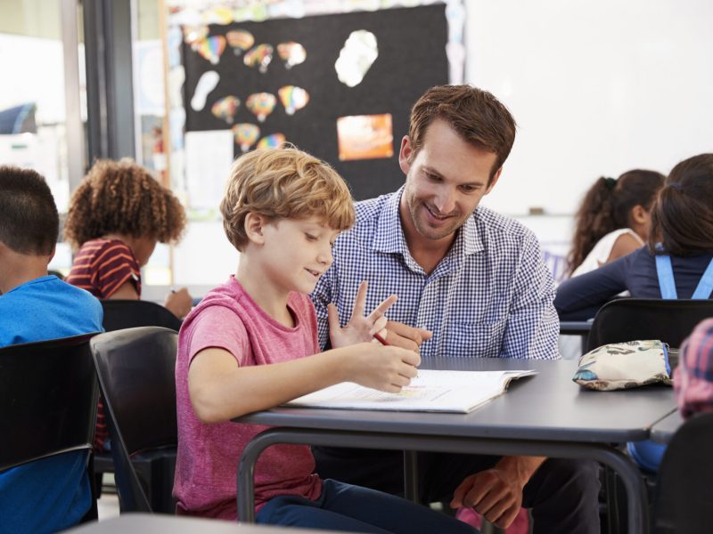 Teacher and young school boy looking at notebook in class