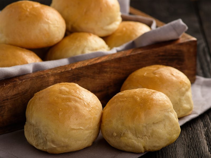 Homemade potato bread rolls on wooden tray.