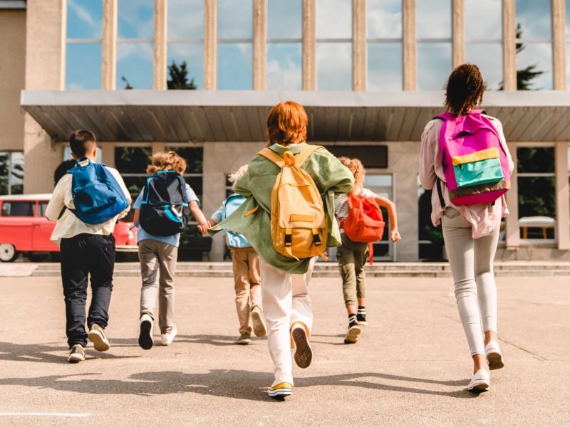 Little kids schoolchildren pupils students running hurrying to the school building for classes lessons from to the school bus. Welcome back to school. The new academic semester year start